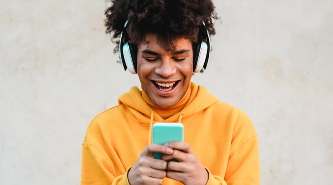 A happy young adult with headphones on smiling down at his phone