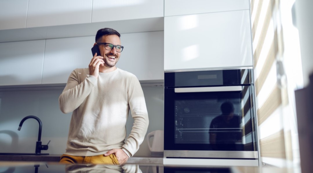 Man in the kitchen on phone smiling looking out the window