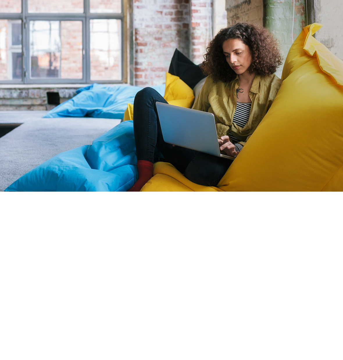 Woman sitting on a stack of bean bags looking at her laptop