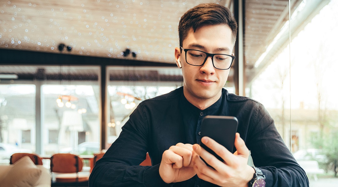 Man with glasses looking happily down at his phone
