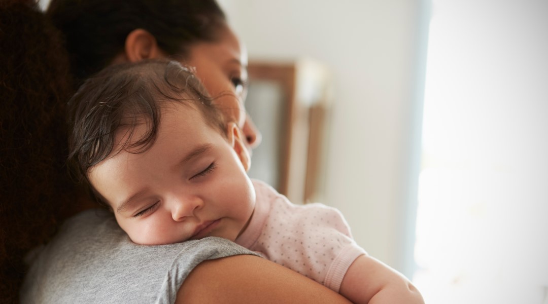 Cute baby sleeping on her mothers shoulder