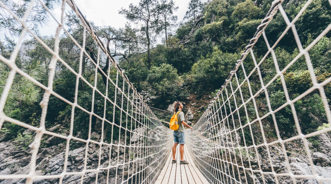 Young woman crossing a suspension bridge over mountain stream.